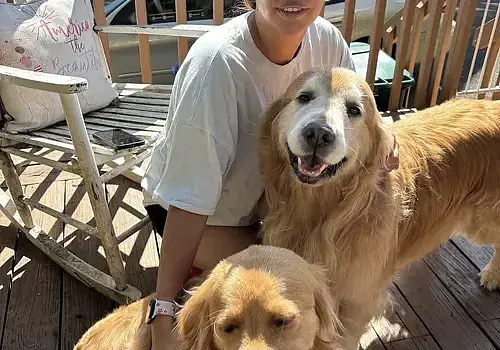 Romina sits on the deck with her dogs in a backyard maintained by Dog Butler.